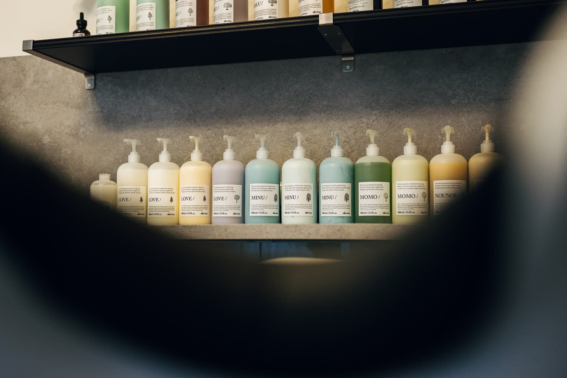 Reihe pastellfarbener Davines-Pflegeflaschen auf grauem Regal im Salon Charles Edward
