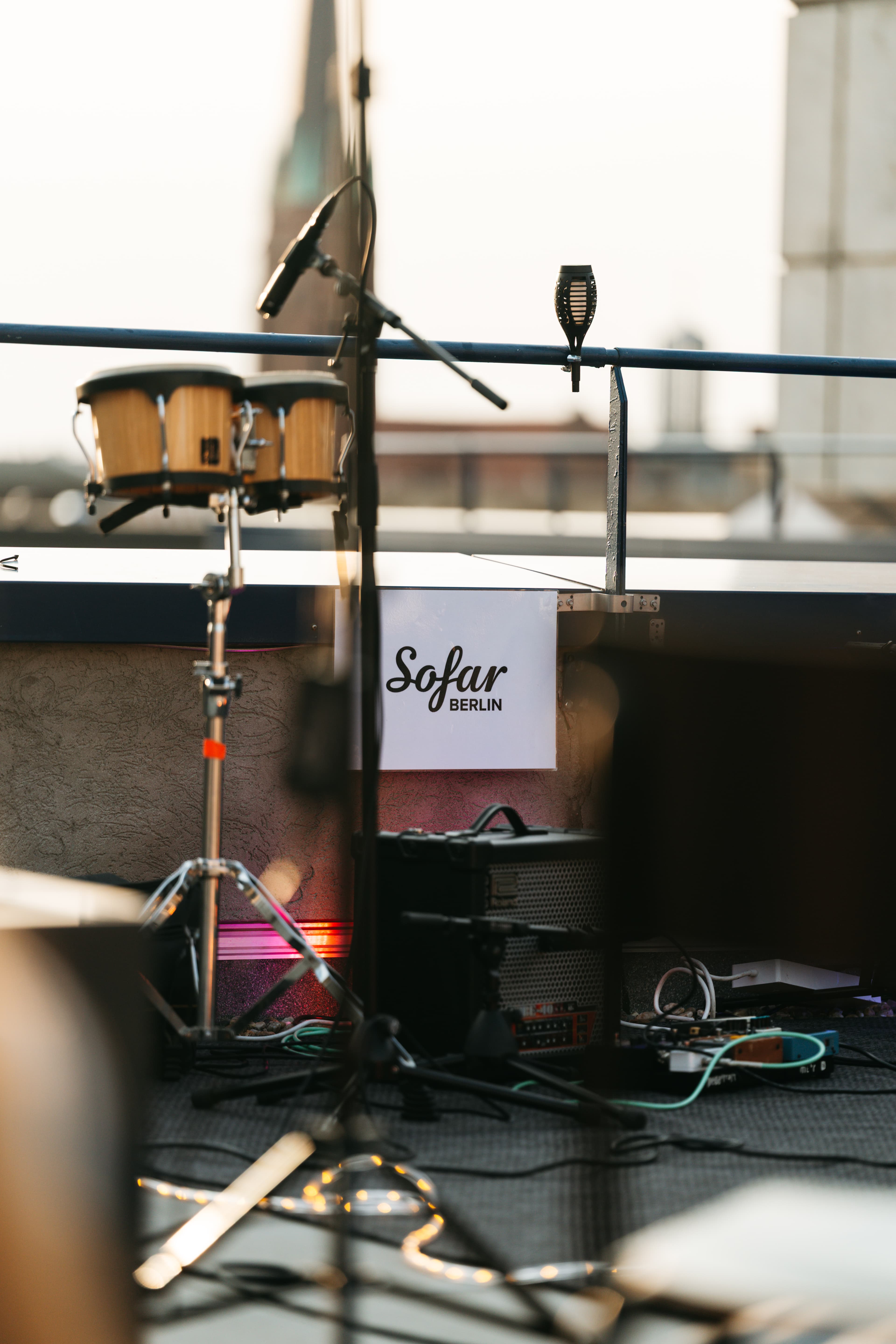 Bühne auf dem Dach: Bongos, Mikrofon und Amp vor Sofar-Berlin-Schild und Berlin-Skyline bei Golden Hour