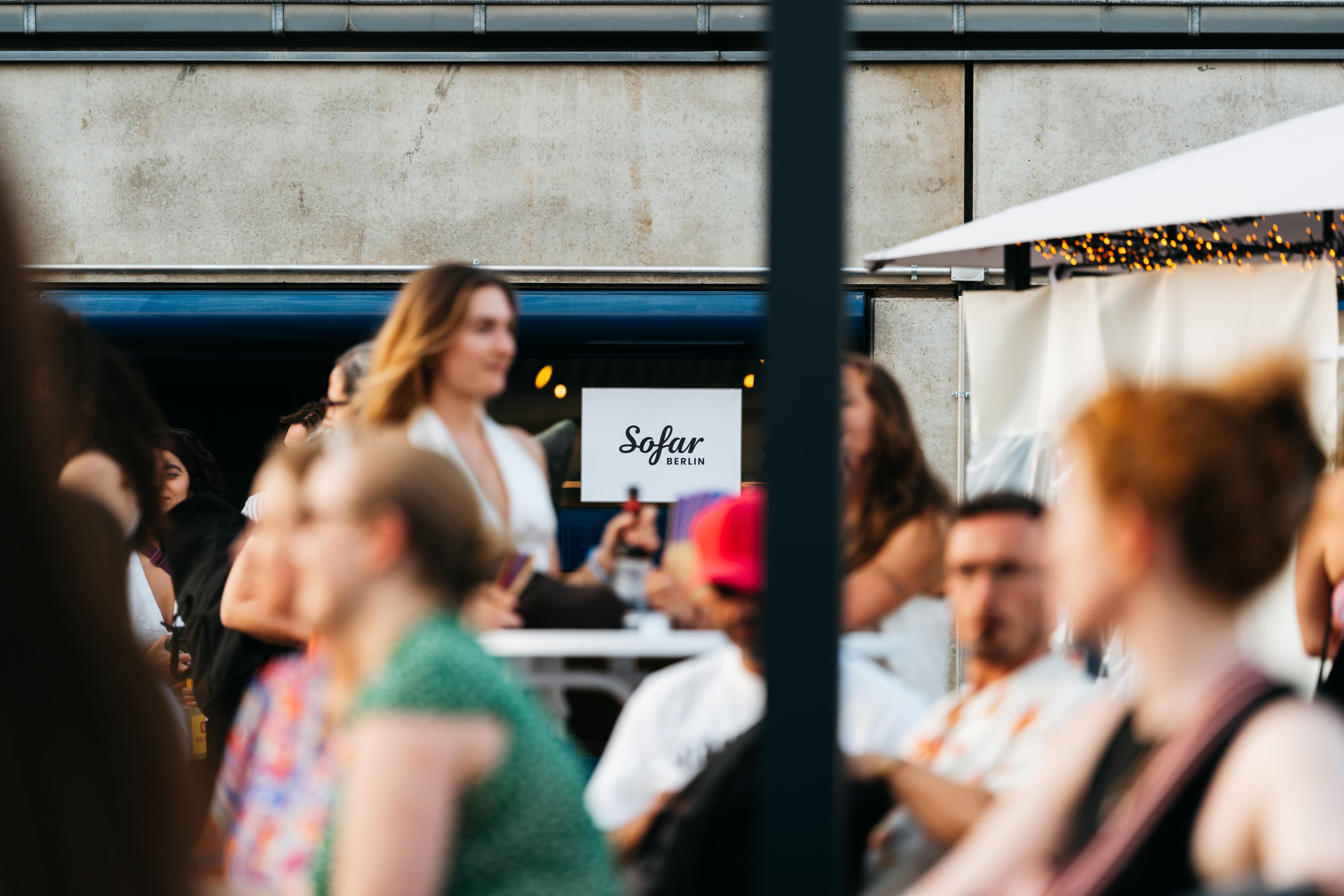 Gäste beim Sofar-Abend in Moabit, Sofar-Berlin-Schild im Fokus, Lichterketten am Zelt